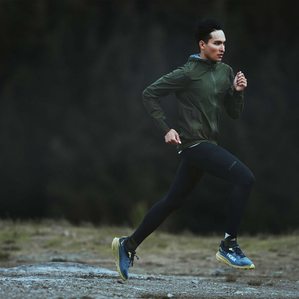 Front view of a model wearing the GOREWEAR Men's Concurve Tights in the Black colourway. Model is also wearing shoes, socks and a jacket, and is in a running motion. (8503998611618)