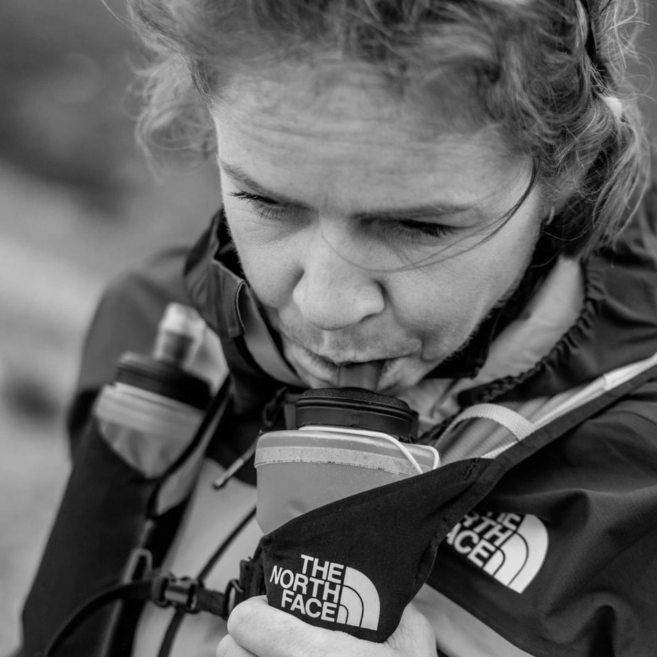 Someone drinking from a Maurten Drinkflask in the 550 ml size. The Drinkflask is being carried in the front pocket of a hydration vest. (8560930324642)