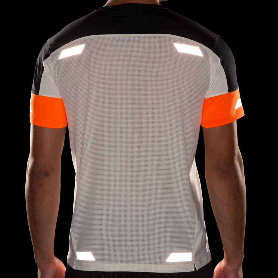 Back view of a model wearing the Brooks Men's Run Visible Short Sleeve 2.0 in the Ecru/Fluoro Flash/Black colourway. Reflective strips are reflecting artificial light. (8499431800994)