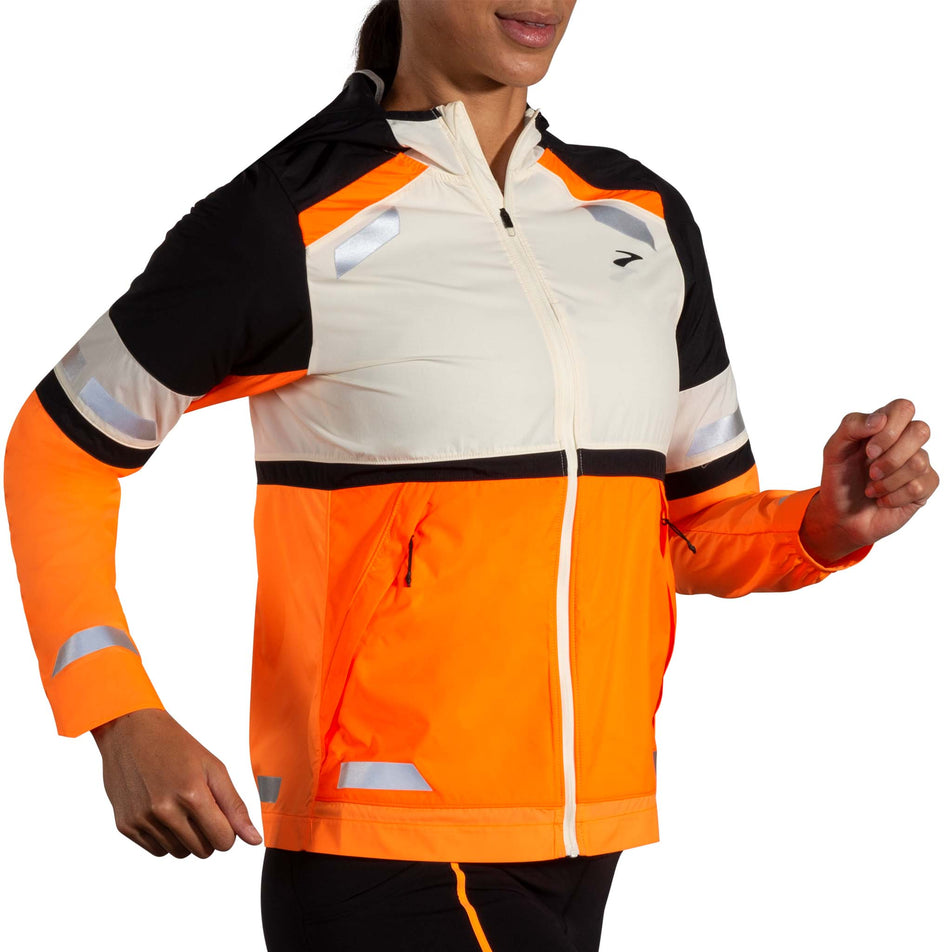 Front view of a model wearing the Brooks Women's Run Visible Jacket 2.0 in the Ecru/Fluoro Flash/Black colourway. Model is also wearing black Brooks tights. (8499442024610)