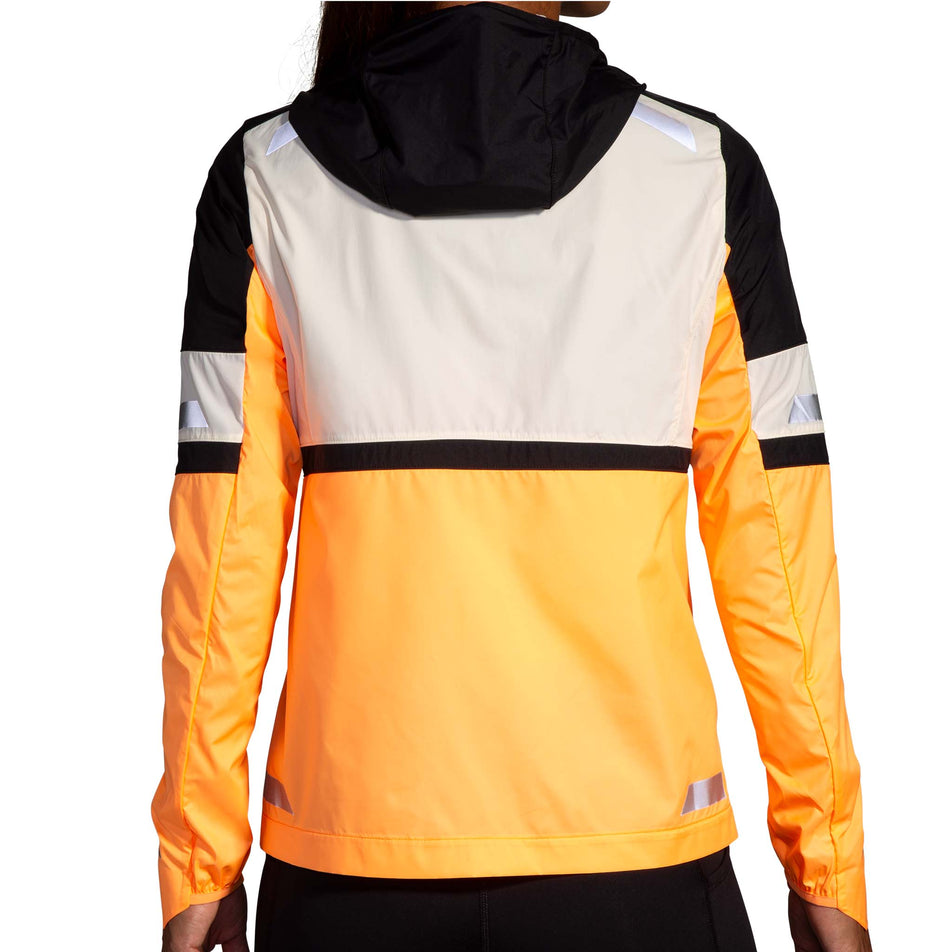 Back view of a model wearing the Brooks Women's Run Visible Jacket 2.0 in the Ecru/Fluoro Flash/Black colourway. Model is also wearing black Brooks tights. (8499442024610)