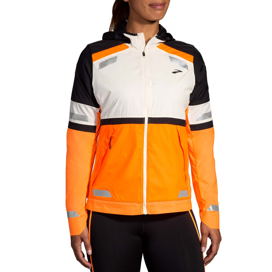 Front view of a model wearing the Brooks Women's Run Visible Jacket 2.0 in the Ecru/Fluoro Flash/Black colourway. Model is also wearing black Brooks tights.(8499442024610)