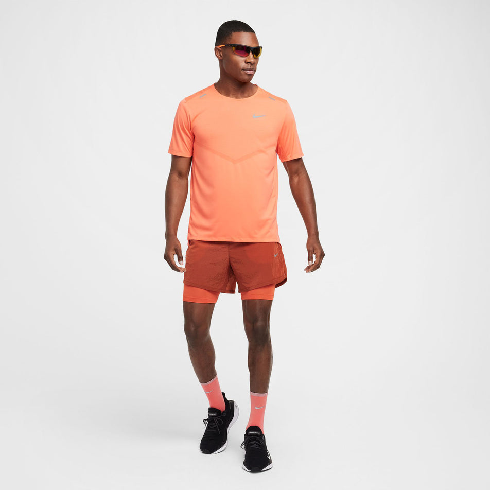 Front view of a model wearing the Nike Men's Dri-FIT Rise 365 Short-Sleeve Running Top in the LT Wild Mango/Reflective Silv colourway. Model is also wearing Nike shorts, socks, and shoes. (8497729110178)