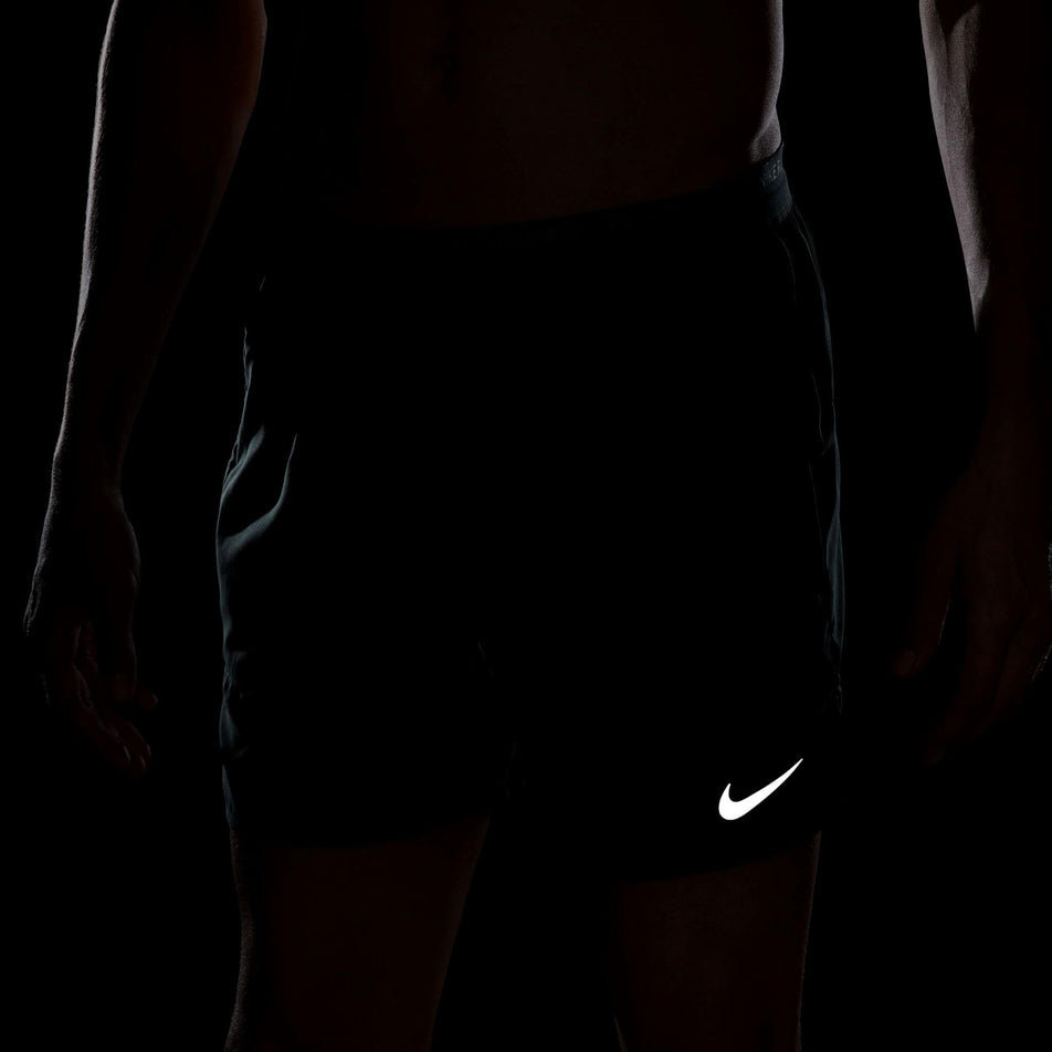 The reflective Nike Swoosh on the front of a pair of Nike in the Men's Stride Dri-FIT 5