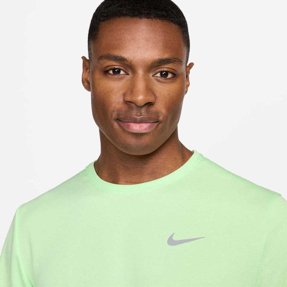 Close-up front view of a model wearing a Nike Men's Miler Dri-FIT UV Short-Sleeve Running Top in the Vapor Green/Reflective Silv colourway. Only the upper part of the top can be seen in the image. (8399203467426)