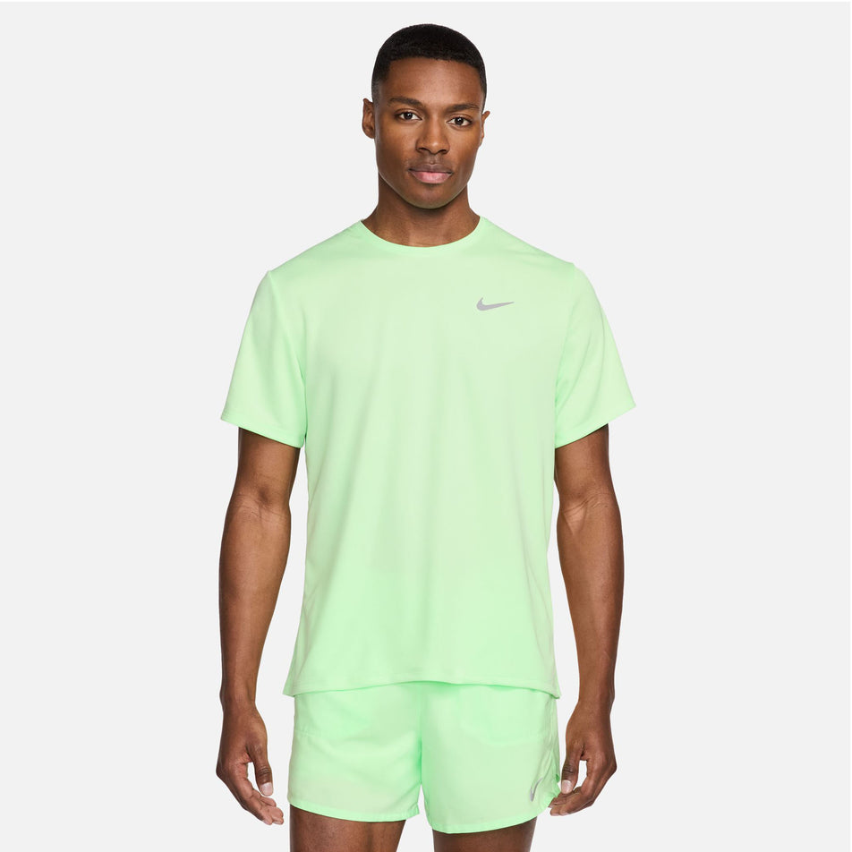 Front view of a model wearing a Nike Men's Miler Dri-FIT UV Short-Sleeve Running Top in the Vapor Green/Reflective Silv colourway. Model is also wearing Nike running shorts. (8399203467426)