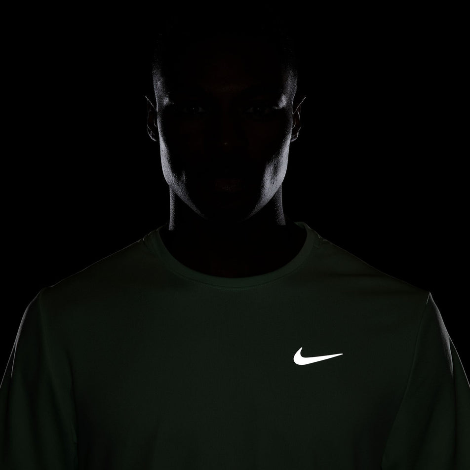 Front view of the reflective Nike SWOOSH on a Nike Men's Miler Dri-FIT UV Short-Sleeve Running Top in the Vapor Green/Reflective Silv colourway. Top is being worn by a model. (8399203467426)