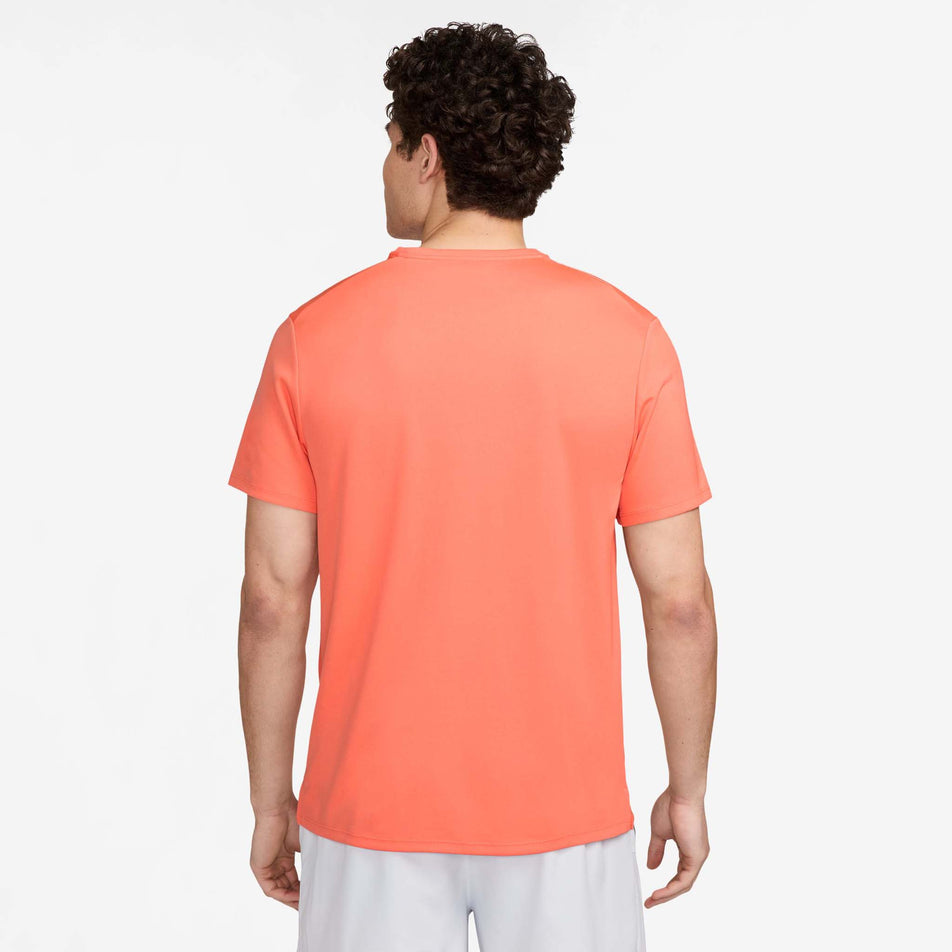 Back view of a model wearing the Nike Men's Miler Dri-FIT UV Short-Sleeve Running Top in the LT Wild Mango/Reflective Silv colourway. Model is also wearing white Nike shorts. (8497716560034)