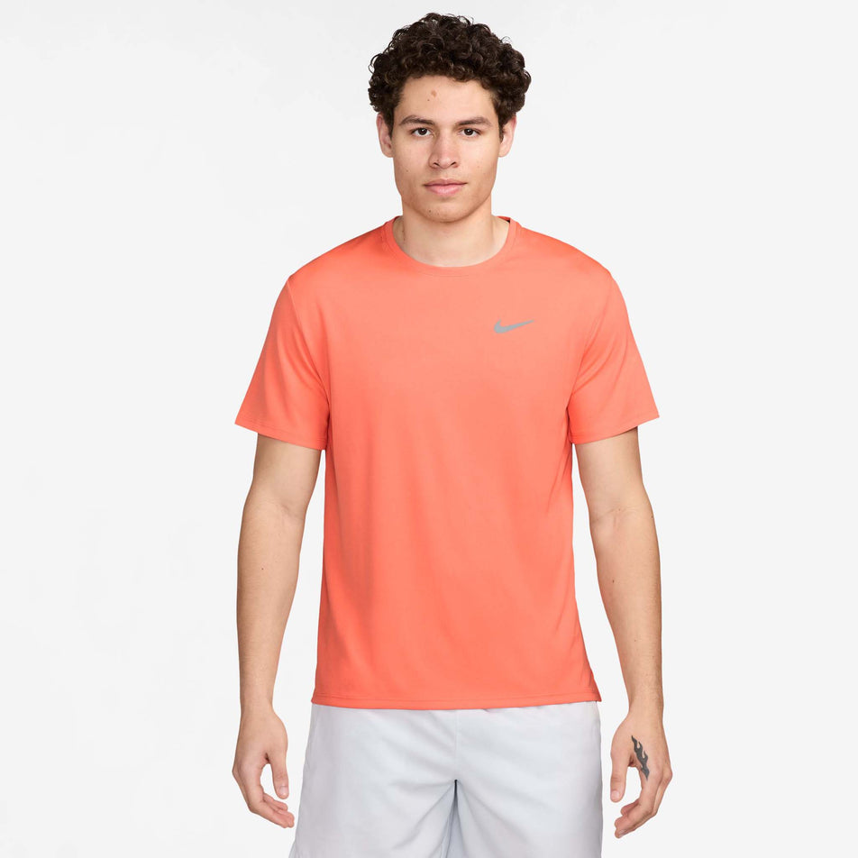 Front view of a model wearing the Nike Men's Miler Dri-FIT UV Short-Sleeve Running Top in the LT Wild Mango/Reflective Silv colourway. Model is also wearing white Nike shorts. (8497716560034)