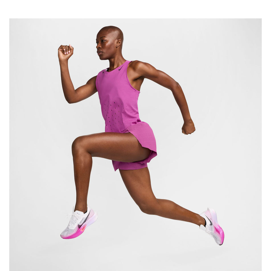 Side view of a model wearing a Nike Women's AeroSwift Dri-FIT ADV Running Singlet in the Hot Fuchsia/Black colourway. Model is also wearing Nike shorts and shoes, and is in a running pose. (8492375015586)