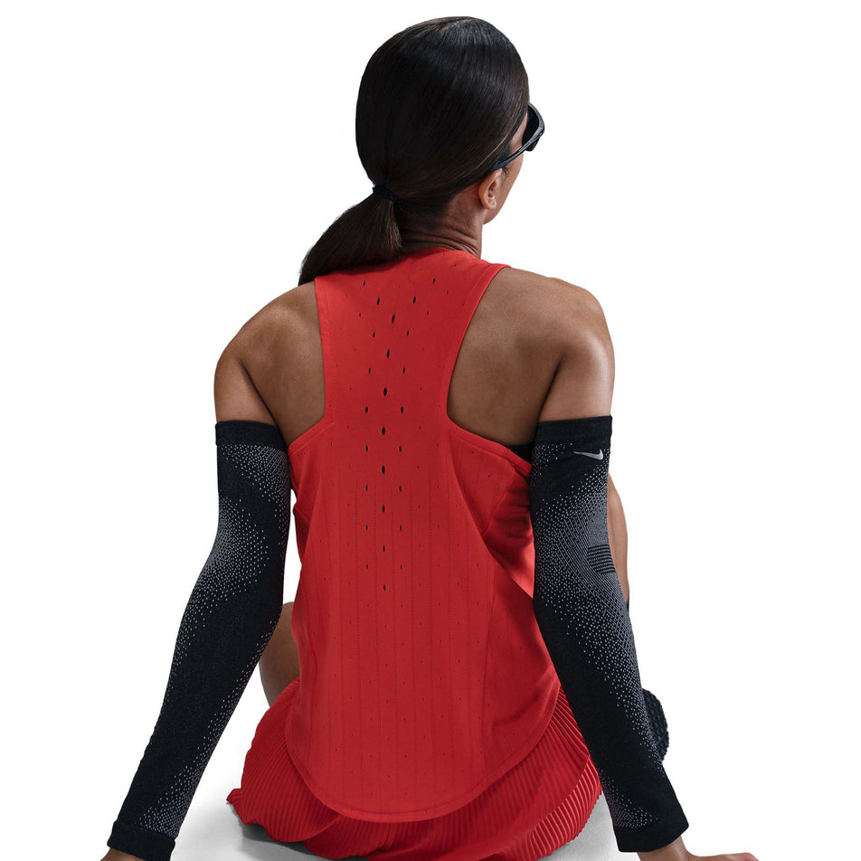 Back view of a model wearing a Nike Women's AeroSwift Dri-FIT ADV Running Singlet in the Lt Crimson/Black colourway. Model is also wearing sunglasses, arm sleeves, and shorts. (8562048630946)