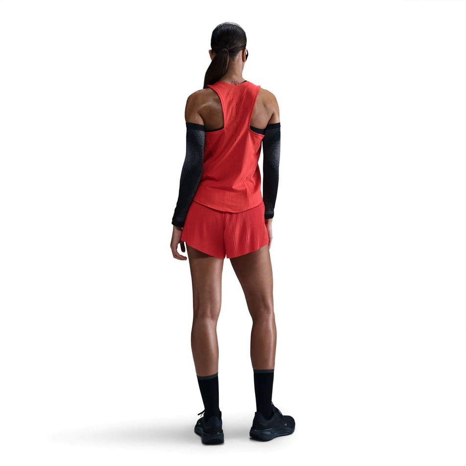 Back view of a model wearing a Nike Women's AeroSwift Dri-FIT ADV Running Singlet in the Lt Crimson/Black colourway. Model is also wearing sunglasses, arm sleeves, shorts, socks and shoes.  (8562048630946)