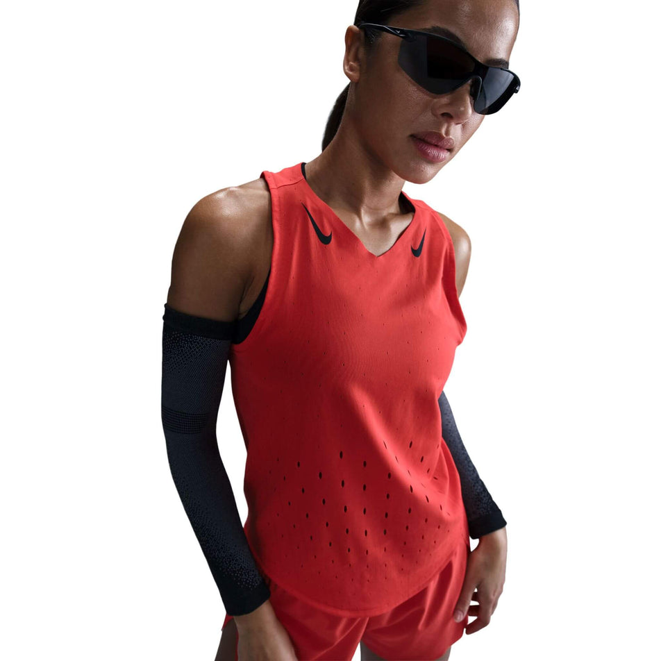 Front view of a model wearing a Nike Women's AeroSwift Dri-FIT ADV Running Singlet in the Lt Crimson/Black colourway. Model is also wearing sunglasses, arm sleeves, and shorts. (8562048630946)