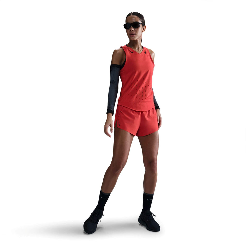 Front view of a model wearing a Nike Women's AeroSwift Dri-FIT ADV Running Singlet in the Lt Crimson/Black colourway. Model is also wearing sunglasses, arm sleeves, shorts, socks and shoes.  (8562048630946)