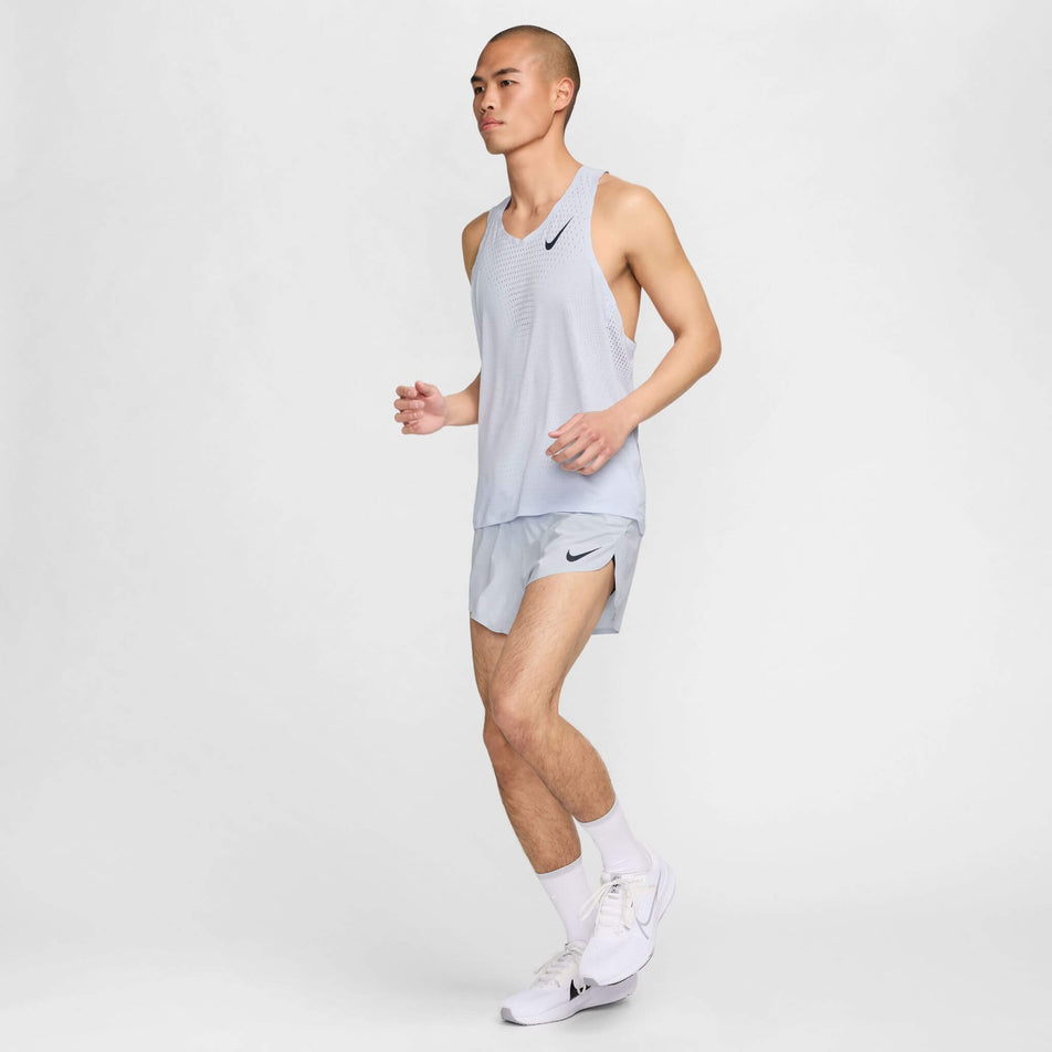 A model wearing a Nike Men's AeroSwift Dri-FIT ADV Running Singlet in the Football Grey/Dark Obsidian colourway. Model is also wearing Nike running shorts, socks and shoes, and is in a running pose. (8399202058402)