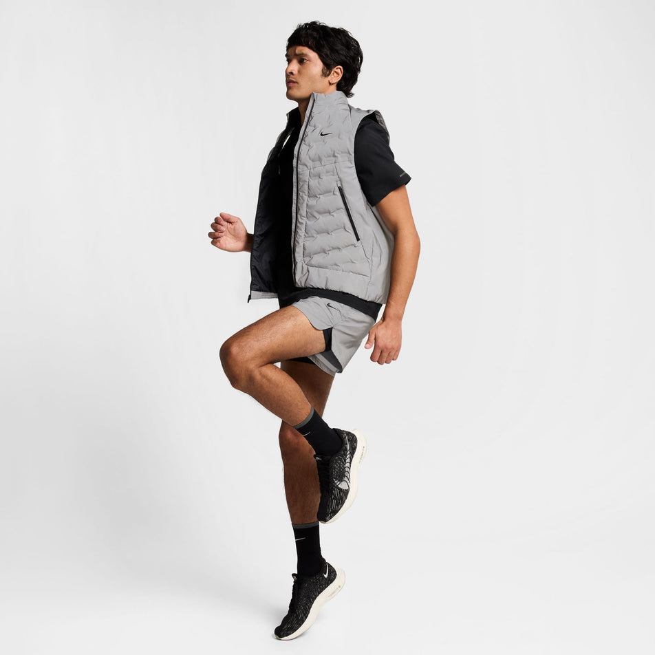 Front left side view of a model wearing the Nike Men's Therma-FIT Running Division ADV Running Vest. Model is also wearing shorts, a t-shirt, socks and shoes, and is in a running pose. (8497736941730)