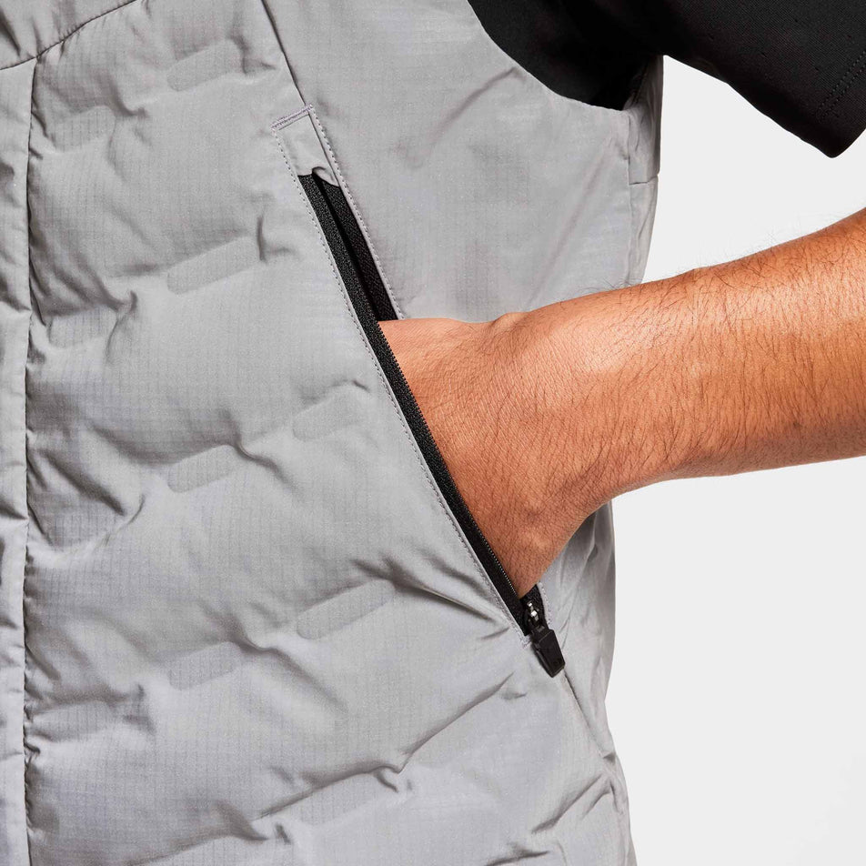 Close-up view of a model demonstrating the left zippered hand pocket on the Nike Men's Therma-FIT Running Division ADV Running Vest. Top is being worn by a model. (8497736941730)