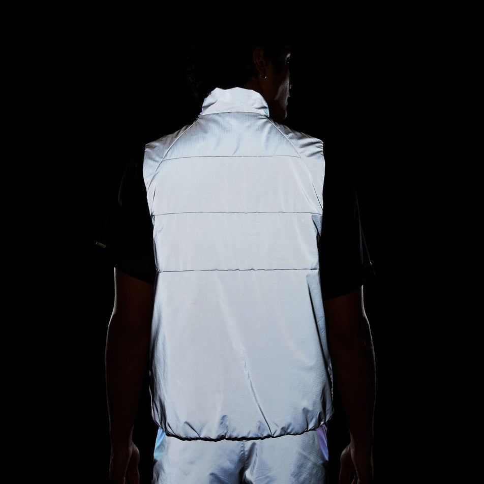 Back view of a model wearing the Nike Men's Therma-FIT Running Division ADV Running Vest in the dark, allowing the reflectivity to show.  (8497736941730)