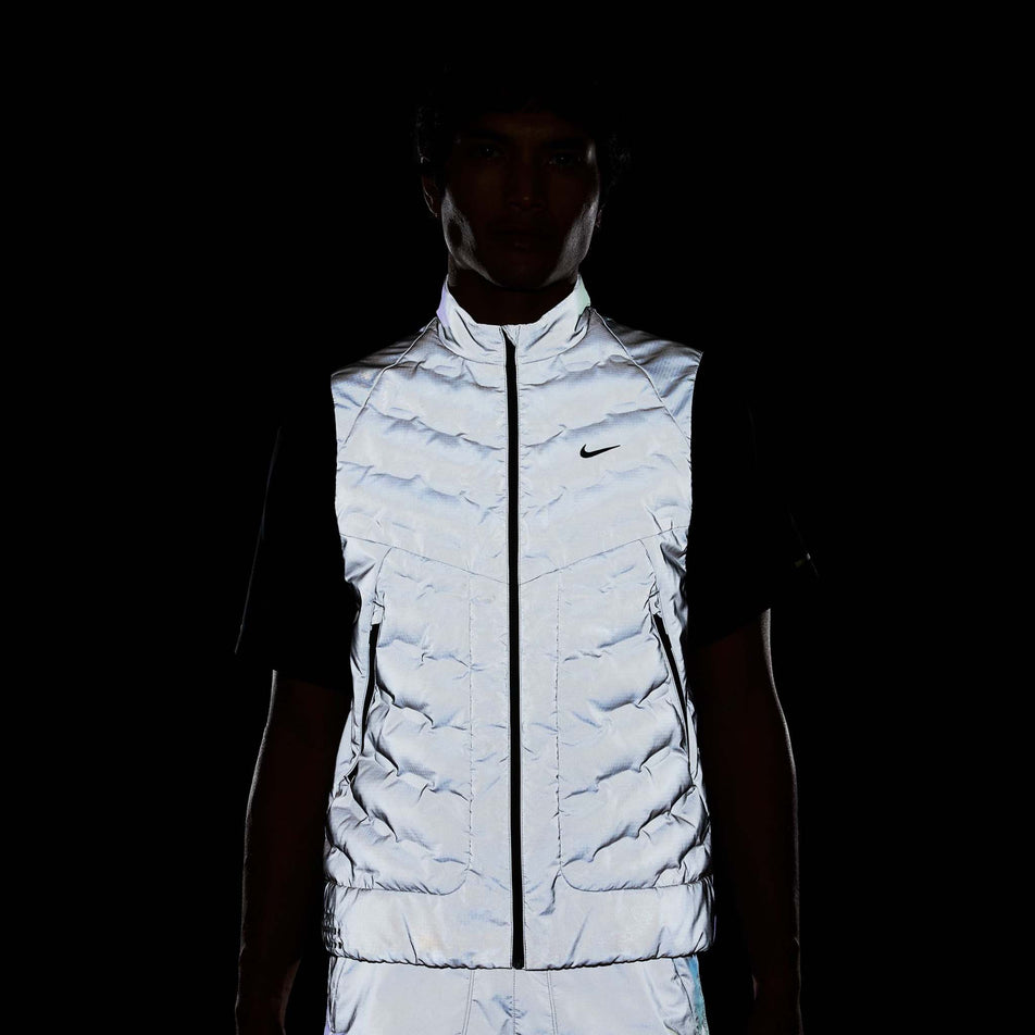 Front view of a model wearing the Nike Men's Therma-FIT Running Division ADV Running Vest in the dark, allowing the reflectivity to show. (8497736941730)