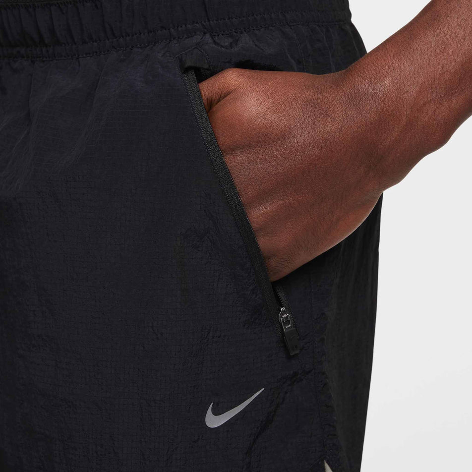 Close-up of a model demonstrating the left zip hand pocket on the Nike Men's Dri-FIT Water-Repellent Running Division Stride 5