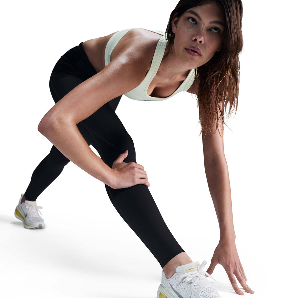 Angled view of a model wearing a pair of Nike Women's Swift Dri-FIT High Rise 7/8 Running Tights in the Black/Reflective Silver colourway. (8560773759138)