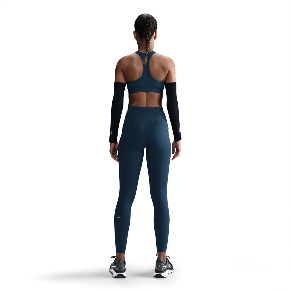 Back view of a model wearing a pair of Nike Women's Swift Dri-FIT High Rise 7/8 Running Tights in the Armory Navy/Reflective Silver colourway. (8560458563746)