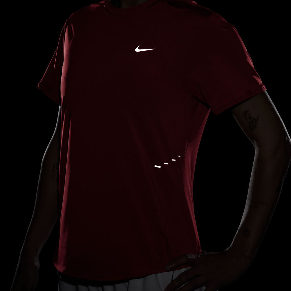 The reflective Nike SWOOSH and reflective graphics on the front of a Nike Women's Swift Dri-FIT Short-Sleeve Running Top in the Light Crimson/Reflective Silver. (8560485662882)