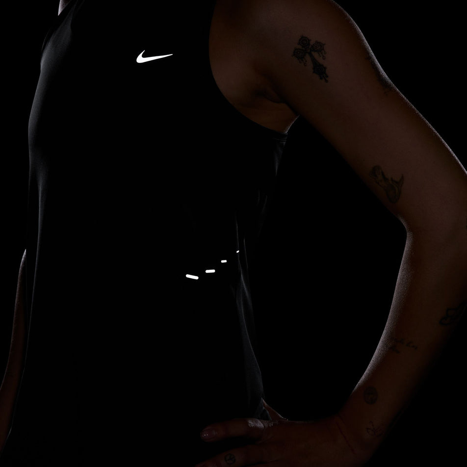 The reflective Nike SWOOSH and reflective graphics on the front of a Nike Women's Swift Dri-FIT Running Tank Top in the Black/Reflective Silver colourway.  (8560470524066)