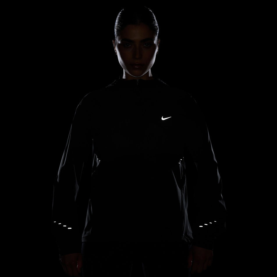 The reflective Nike SWOOSH and reflective graphics on a Nike Women's Swift Repel Packable Running Jacket in the Black/Reflective Silver colourway.  (8560817635490)