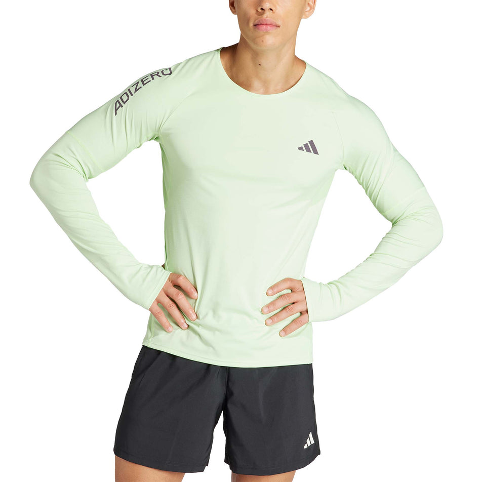 Front view of a model wearing an adidas Men's Adizero Running Long Sleeve Top in the Semi Green Spark/Aurora Black colourway. Model is also wearing adidas running shorts. (8312060969122)