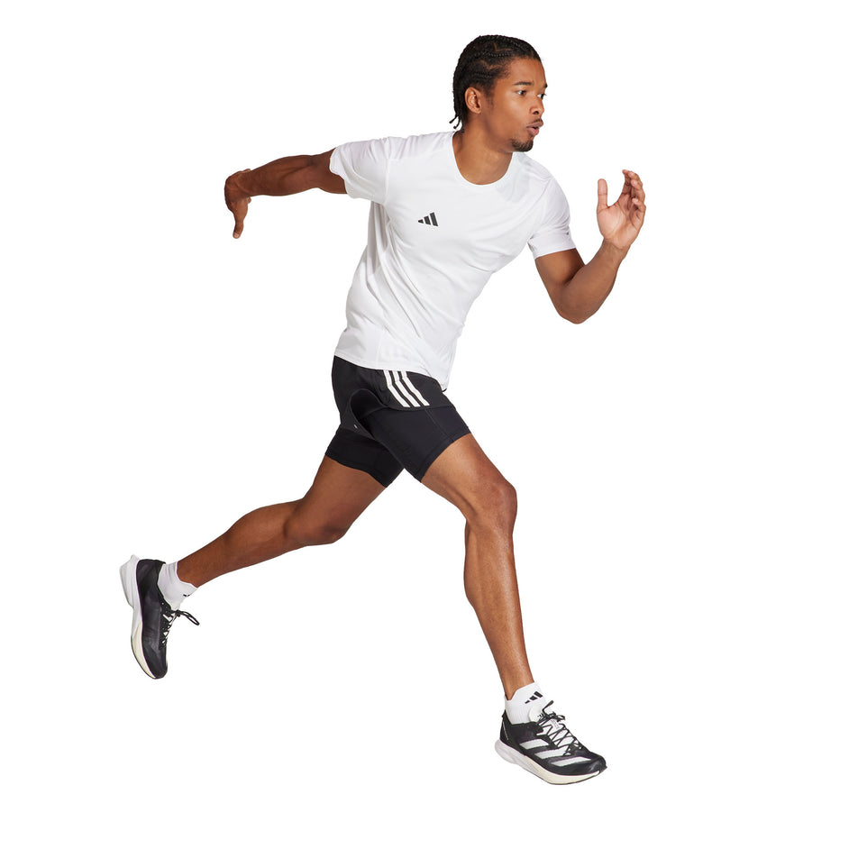 A model wearing a pair of adidas Men's Own The Run 3-Stripes 2-In-1 Shorts in the black colourway. Model is also wearing socks, shoes and a top, and is in a running pose. (8449469448354)