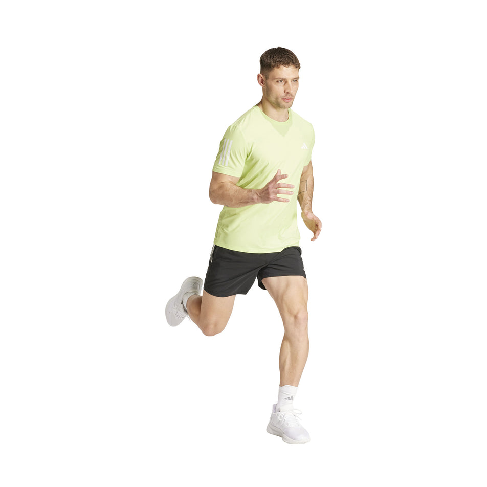 Front view of a model wearing an adidas Men's Own The Run T-Shirt in the Pulse Lime colourway. Model is also wearing adidas shorts, socks and shoes, and is in a running pose. (8457446949026)