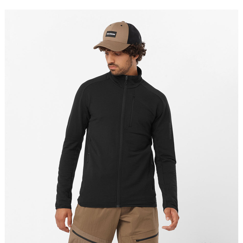 Front view of a model wearing a Salomon Men's Essential Lightwarm Full Zip Midlayer Jacket in the Deep Black colourway. Model is also wearing legwear and a cap. (8464264200354)