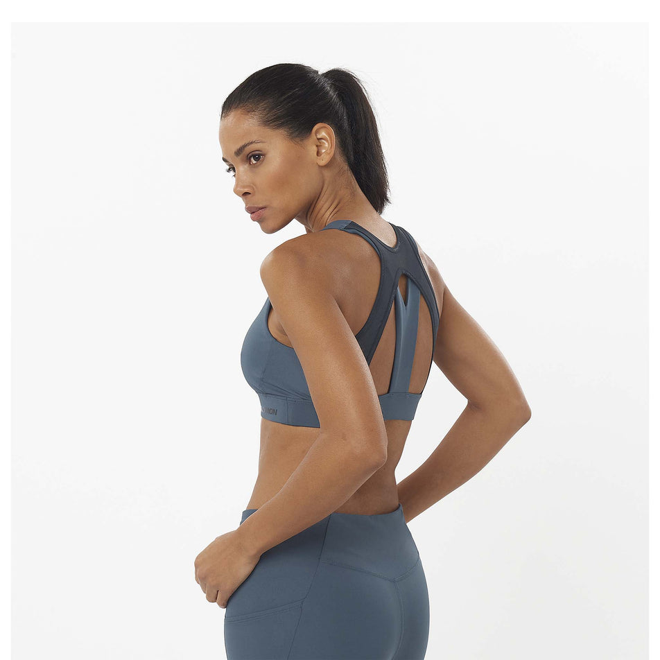 Angled, back view of a model wearing a Salomon Women's Cross Run Sports Bra in the Midnight Navy/Deep Black colourway. Model is also wearing leggings. (8463080816802)