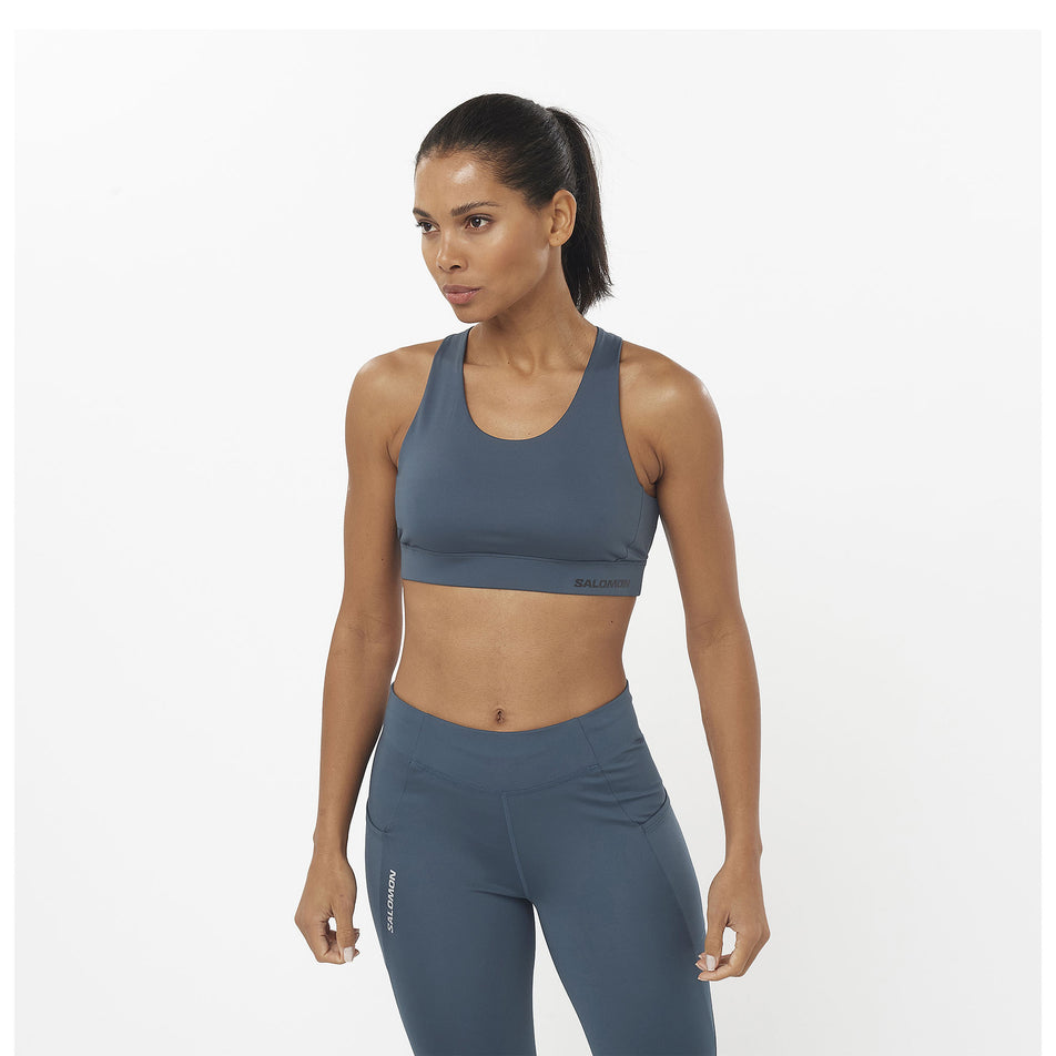 Front view of a model wearing a Salomon Women's Cross Run Sports Bra in the Midnight Navy/Deep Black colourway. Model is also wearing leggings. (8463080816802)