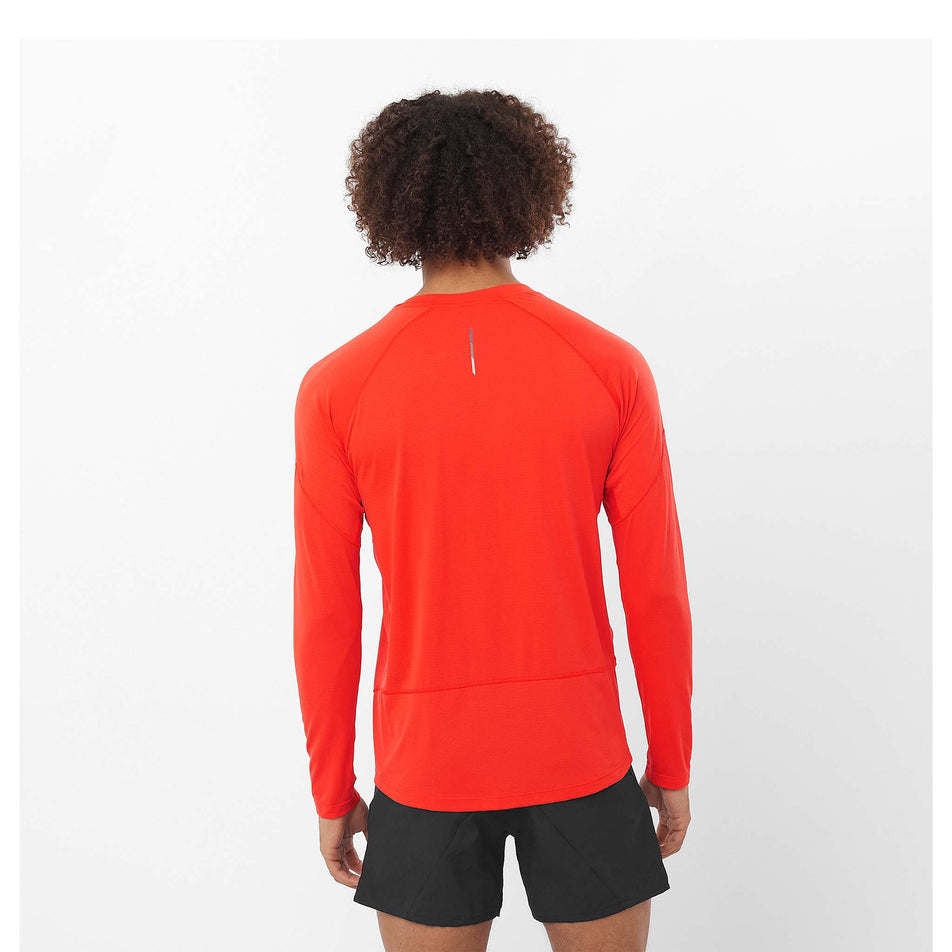 Back view of a model wearing a Salomon Men's Cross Run Long Sleeve T-Shirt in the Cherry Tomato colourway. Model is also wearing sunglasses and shorts. (8467287179426)