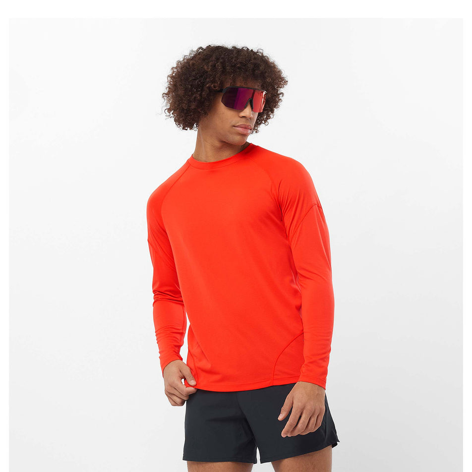 Front view of a model wearing a Salomon Men's Cross Run Long Sleeve T-Shirt in the Cherry Tomato colourway. Model is also wearing sunglasses and shorts. (8467287179426)