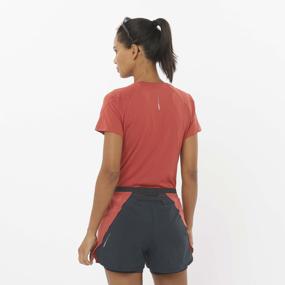 Back view of a model wearing the Salomon Women's Cross Run Short Sleeve T-Shirt in the Tandoori Spice colourway. Model is also wearing shorts and sunglasses. (8509491183778)