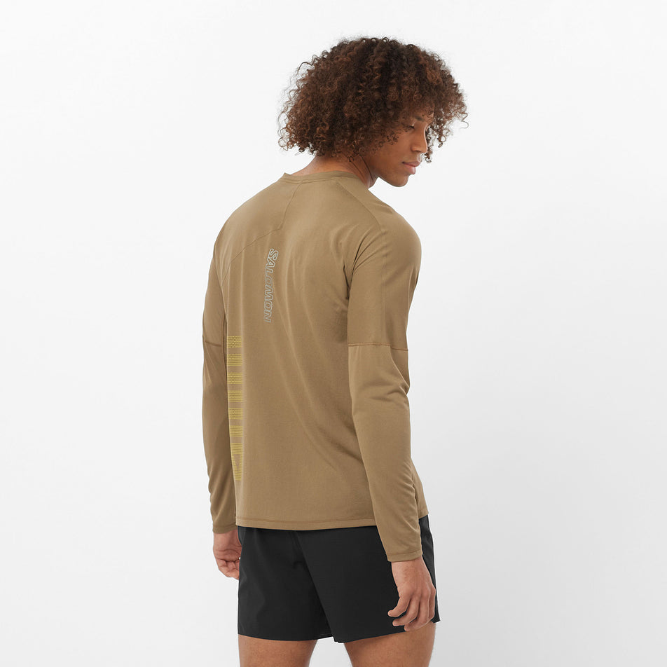 Back view of a model wearing the Salomon Men's Sense Aero Graphic Long-Sleeve T-Shirt in the Shitake/Sulphur Spring colourway. Model is also wearing shorts. (8509586014370)