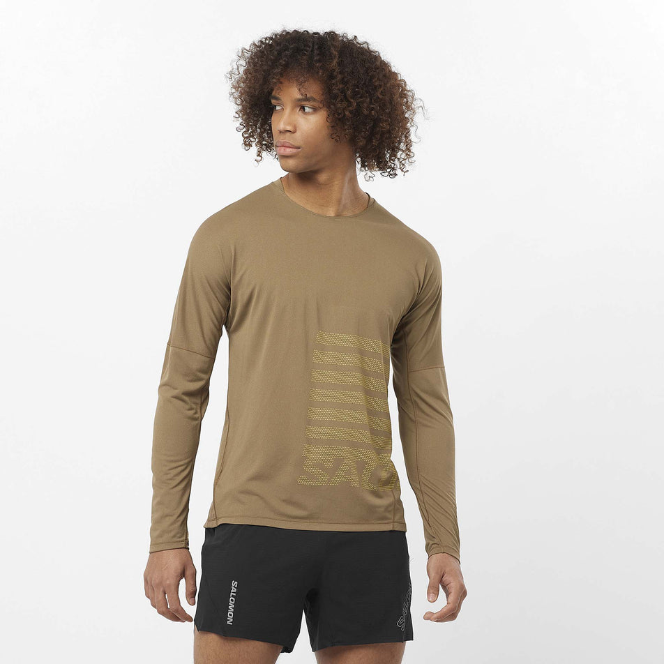 Front view of a model wearing the Salomon Men's Sense Aero Graphic Long-Sleeve T-Shirt in the Shitake/Sulphur Spring colourway. Model is also wearing shorts. (8509586014370)