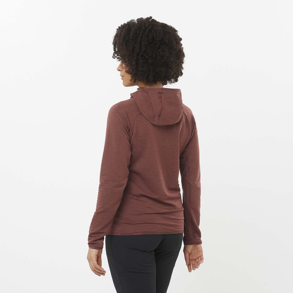 Back view of a model wearing the Salomon Women's Essential Lightwarm Midlayer Jacket Hoodie in the Rum Raisin colourway. Model is also wearing leggings. (8509527097506)