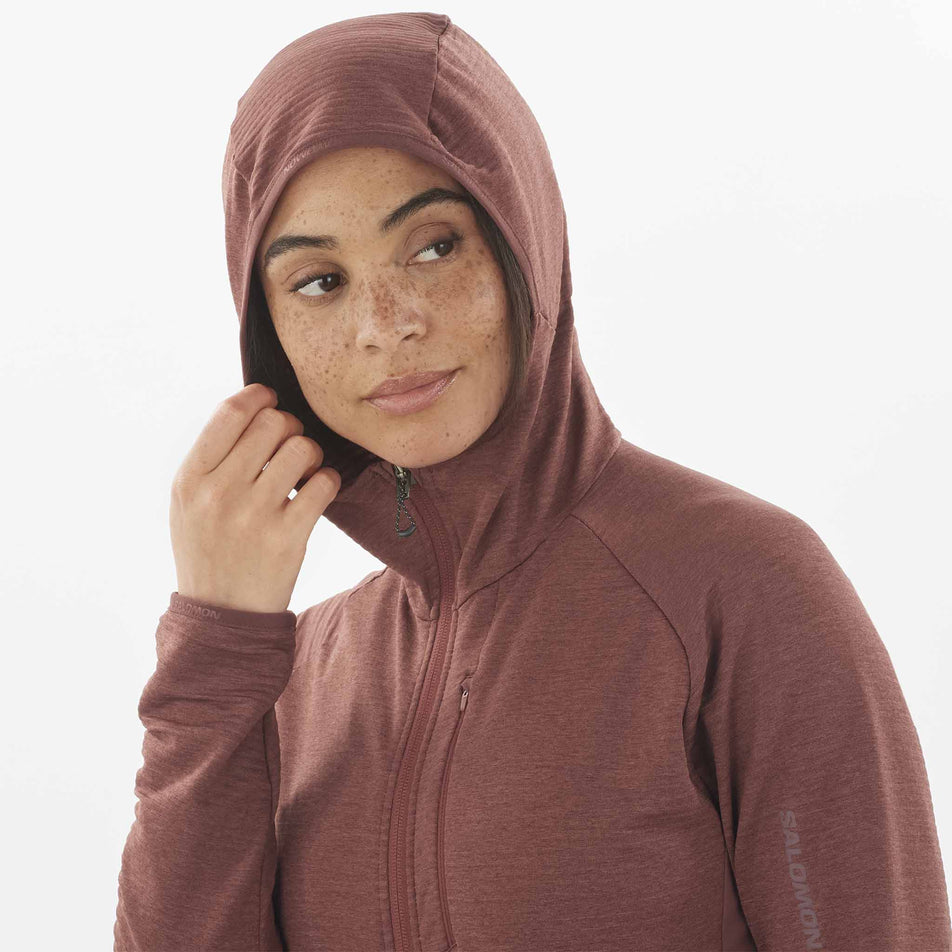 Close-up front view of a model wearing the Salomon Women's Essential Lightwarm Midlayer Jacket Hoodie with the hood up. (8509527097506)