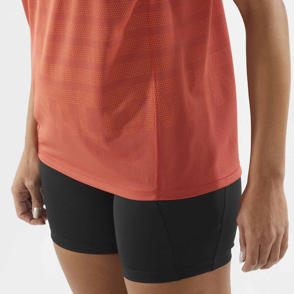 Close-up of the lower-front section of the Salomon Women's Sense Aero Graphic Short Sleeve T-Shirt in the Tandoori Spice/Shocking Orange colourway. Model is also wearing shorts. (8464135618722)