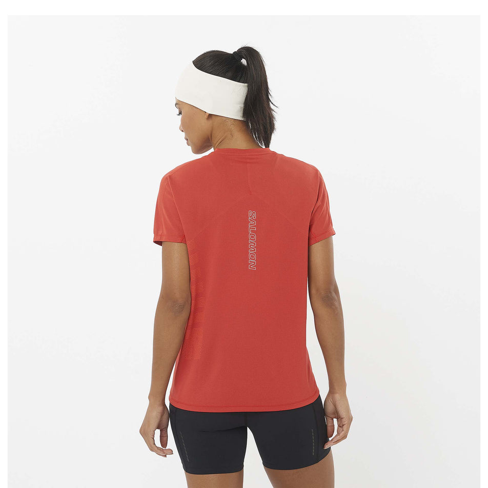 Back view of a model wearing the Salomon Women's Sense Aero Graphic Short Sleeve T-Shirt in the Tandoori Spice/Shocking Orange colourway. Model is also wearing shorts and a headband. (8464135618722)