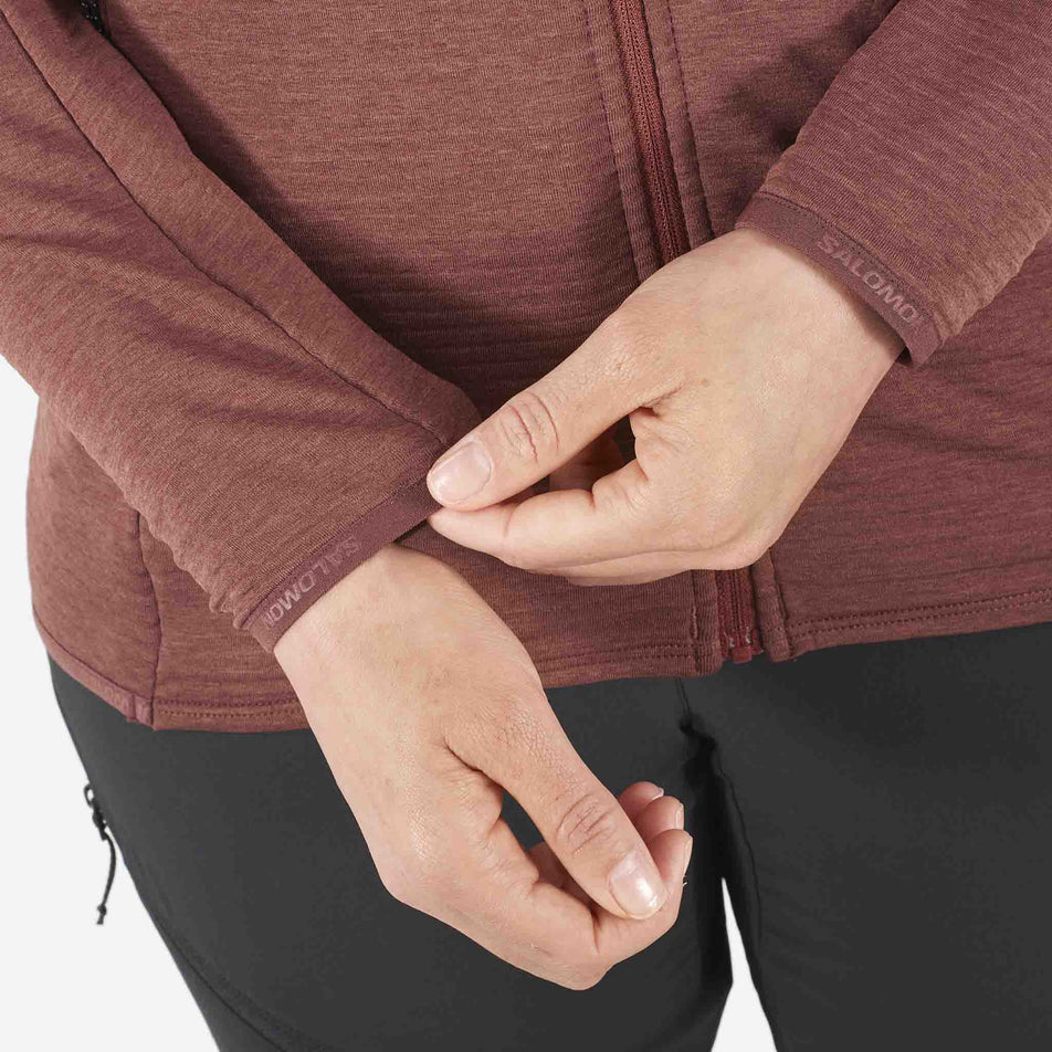 Close-up view of cuffs on the Salomon Women's Essential Lightwarm Full Zip Midlayer Jacket's sleeves. Jacket is being worn by a model who is also wearing leggings. (8509475389602)