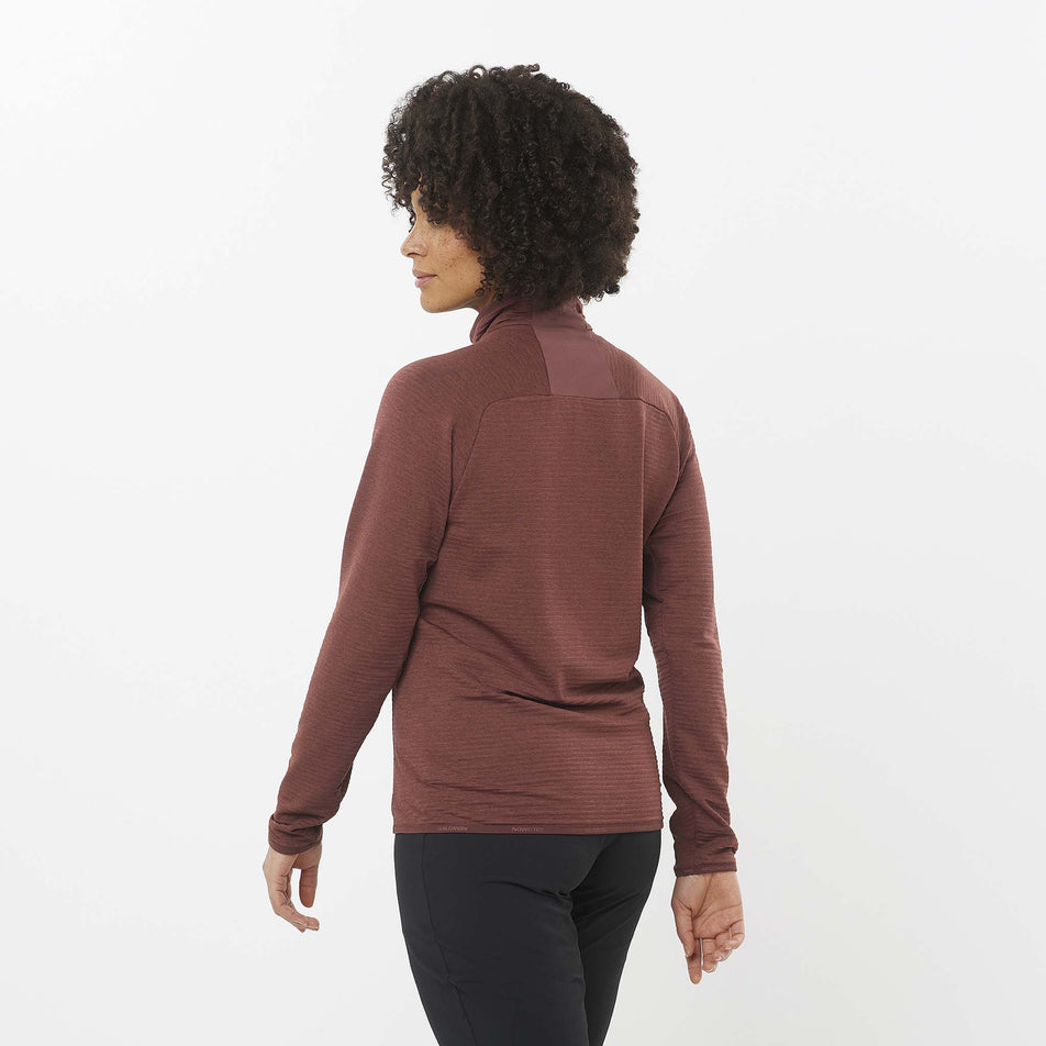 Back view of a model wearing the Salomon Women's Essential Lightwarm Full Zip Midlayer Jacket in the Rum Raisin colourway. Model is also wearing leggings. (8509475389602)