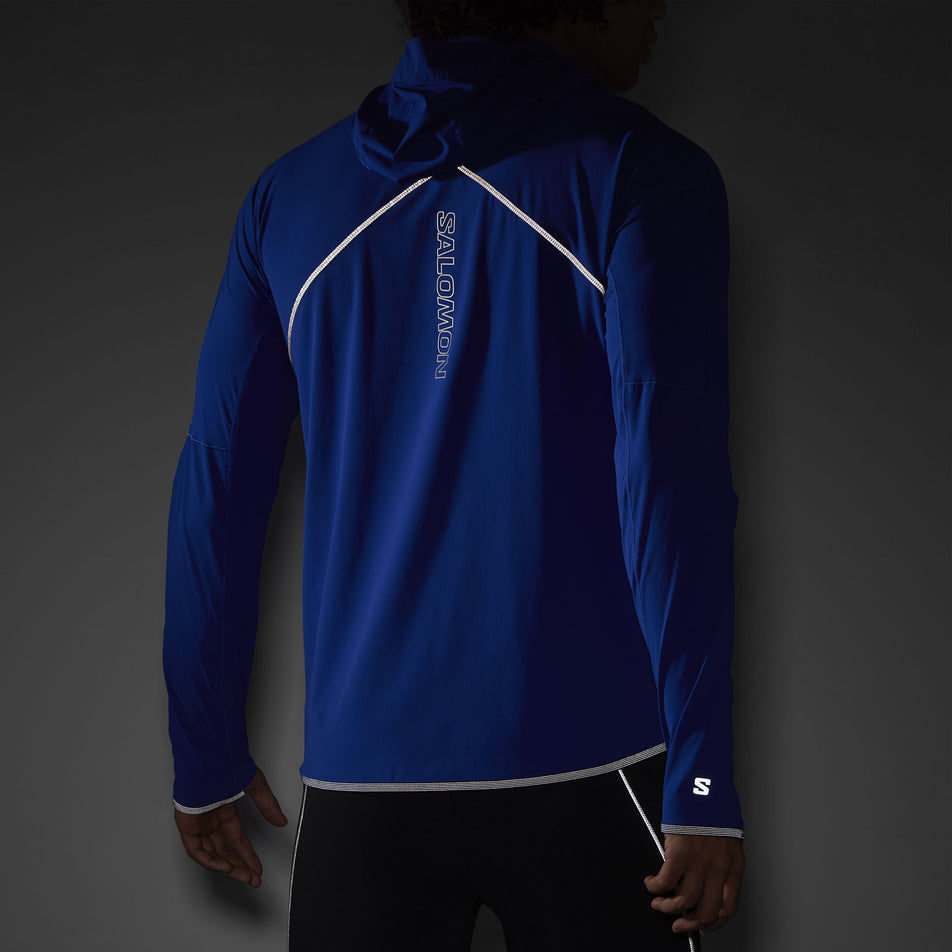 The reflectivity on the back of a Salomon Men's Sense Aero Hybrid Midlayer Jacket with hood in the Surf The Web colourway. Jacket is being worn by a model.  (8464251617442)