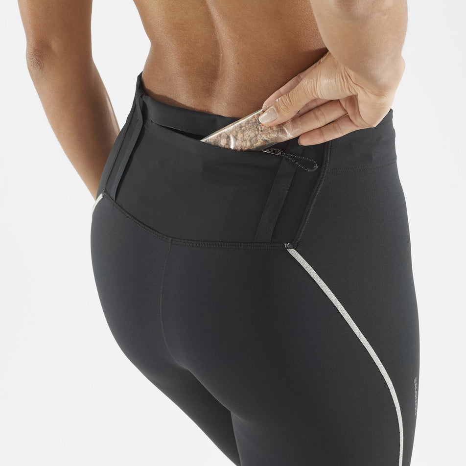 A model demonstrating that nutrition can be stored in the back zip pocket of the Salomon Women's Sense Aero Stow Tights. The tights are being worn by the model. (8509442195618)