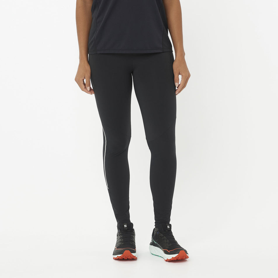 Front view of a model wearing the Salomon Women's Sense Aero Stow Tights in the Deep Black colourway. Model is also wearing a top and running shoes. (8509442195618)