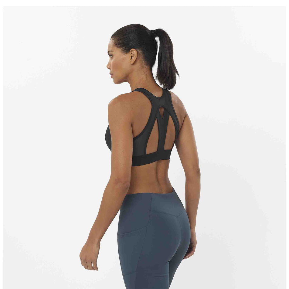 Back view of a model wearing a Salomon Women's Cross Run Sports Bra in the Deep Black colourway. Model is also wearing leggings. (8464178086050)